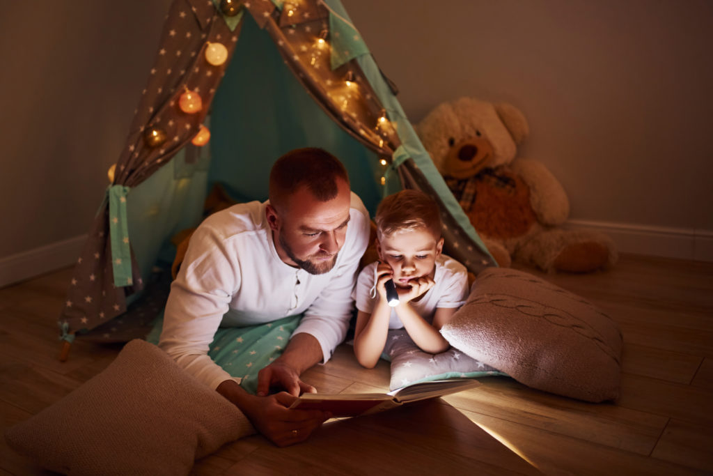 Father and son reading in a cozy tent.